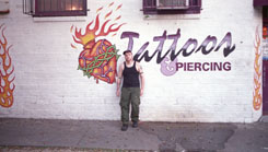 Sir Cornbread of the Needle poses against the painted wall sign outside Cresent City Tattoos where he began as an apprentice and now works full time.