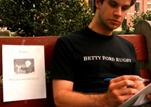 English writing junior Joe Fredo studies in the Peace Quad next to a flyer depicting interim president Rev. William Byron that reads, "Misogyny