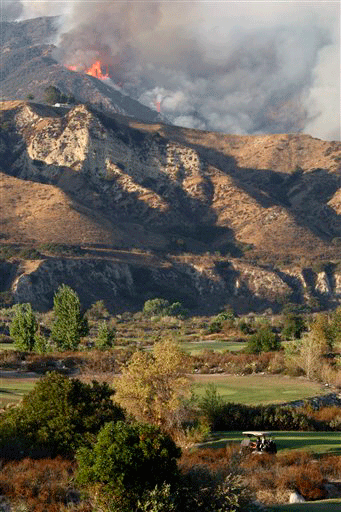 Golfers ride in a golf cart as smoke billows from the Station Fire in the hills behind the Angeles National Golf Coarse in Sunland, Calif. in Los Angeles County on Sunday Aug. 30, 2009. Wildfire threatened 12,000 suburban homes and rained ash on cars as far away as downtown Los Angeles on Sunday, spreading in all directions in hot, dry conditions.