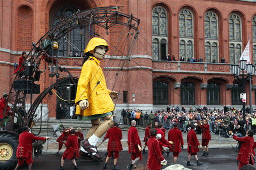 Members of the street theater group Royal De Luxe move a giant marionette in front of the Rote Rathaus in Berlin, Friday, Oct. 2, 2009. The first of a pair of giant marionettes has awakened in Berlin and started the search for her missing partner as part of a massive-scale street performance celebrating German reunification. Clad in a bright yellow rain slicker and hat, the 7.5-meter (25-foot) small giant launched her search early Friday, hung from a crane and accompanied by several dozen hand