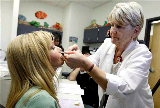 Frontline care providers like nurse Gail Symanik, left, is given the swine flu live virus vaccine nasal mist by nurse practitioner Judy Gallob at the Maricopa Medical Center Thursday, Oct. 8, 2009, in Phoenix. Only healthcare providers will be issued this first-run of the swine flu vaccine, while the general public will be getting the injection version of the vaccine starting next week.