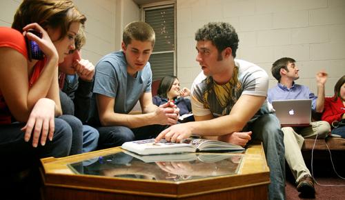 Freshmen Ali Davis, psychology major, Sam Winstrom, mass communication major and Griffen Semple, Jazz Studies major, look on as international business freshman Eli Nasser points out some photos in an old yearbook while relaxing in the Honors floor lounge Tuesday, Jan 12.