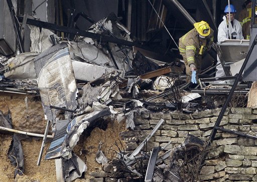 A firefighter places a blue rubber glove on the ground as an investigator, right, looks on by the damaged remains of a small aircraft, left, inside a building, Friday, Feb. 19, 2010, in Austin, Texas. Joseph Stack flew his small airplane Thursday into the building that houses several offices of the Internal Revenue Service.