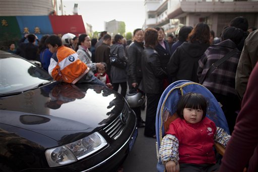 A girl sitting on the back of her mother's bicycle is pushed away by people crowding at the gate of Zhongxin Kindergarten in Taixing in east China's Jiangsu Province Thursday, April 29, 2010. A knife-wielding man attacked the kindergarten class of 4-year-olds Thursday, slashing over two dozen children in what an expert said was a copycat rampage of two other episodes at Chinese schools in the past month. 