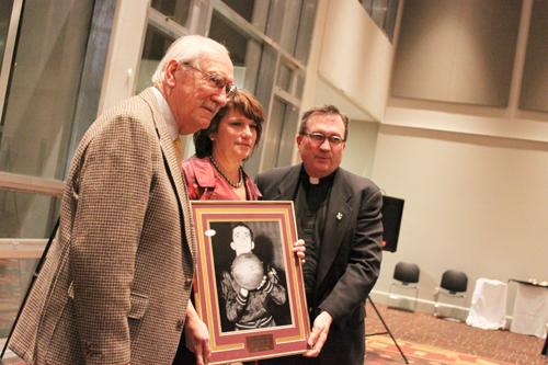 Kylin Casteix Ajubita (center) holds her deceased father’s framed picture that will go on Loyola’s Hall of Fame on Jan. 5. Frank France (left), posing with the Rev. Kevin Wildes S.J. (right), had nominated his friend,  John “Rags” Casteix, Jr., for the recognition. “Rags” received the award 28 years after his death.