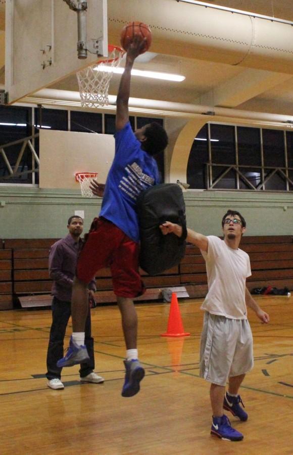 Brandon Dixon does a layup while Ben Aronin, a coach at Elevate New Orleans, blocks him from the side and Sky Hyacinthe, executive director, observes. Students at Elevate New Orleans receive coaching from former professional and semi-professional basketball players.
