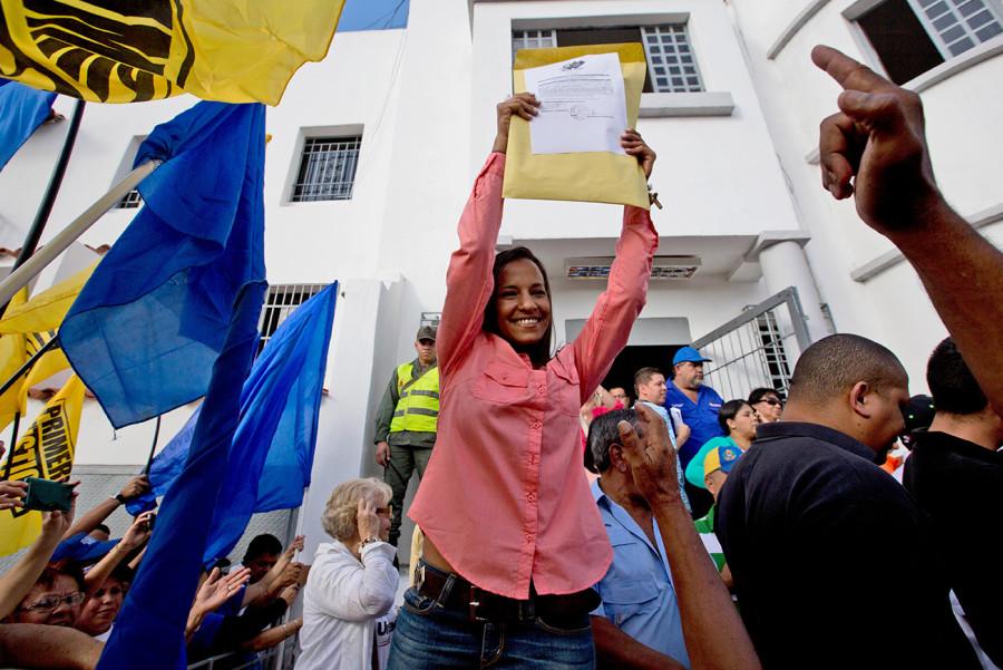 Newly elected opposition congresswoman Marialbert Barrios holds up her credentials as lawmaker, from the National Electoral Council (CNE) in Caracas, Venezuela, Wednesday, Dec. 9, 2015, after congressional elections. The Democratic Unity opposition coalition secured, by a single seat, a two-thirds supermajority, surpassing its even most-optimistic forecasts. (AP Photo/Fernando Llano)