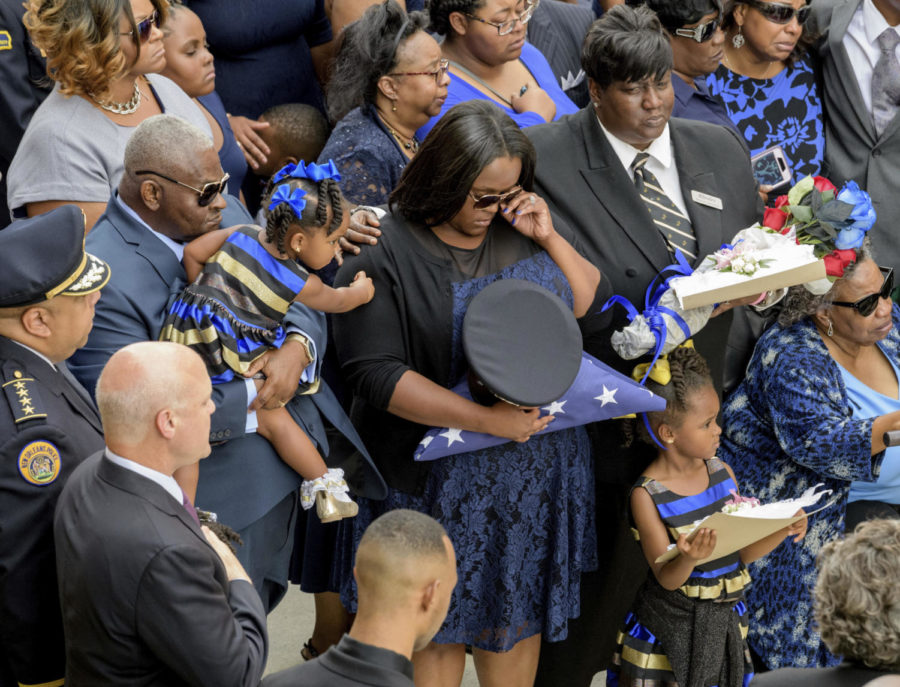 Brittiny McNeil holds the hat and flag of her late husband New Orleans Police Officer Marcus McNeil while she is comforted by her daughter Camille McNeil, 2, left, next to her other daughter, Maisie McNeil, 5, bottom right, and McNeils mother Kimberly McNeil, top right, and his grandmother Alvena McNeil at Mount Olivet Cemetery during his funeral in New Orleans, La., Saturday, Oct. 21, 2017. New Orleans Police Department Superintendent Michael Harrison, left, and Mayor Mitch Landrieu, second left, stand with hands over their hearts. McNeil, 29, was shot and killed Oct. 13 during a routine patrol. (Matthew Hinton/The Advocate via AP) Photo credit: Associated Press