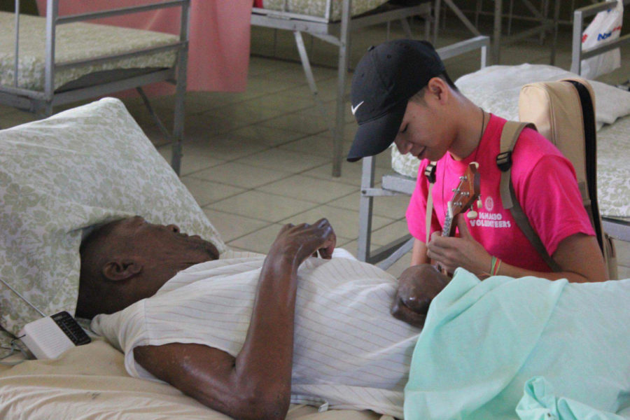 Calvin Tran, music therapy senior, plays ukulele for a patient at St. Teresa's Home for the Destitute and Dying in Kingston, Jamaica, during the Ignacio Volunteer trip December 2017. Photo credit: Lily Cummings