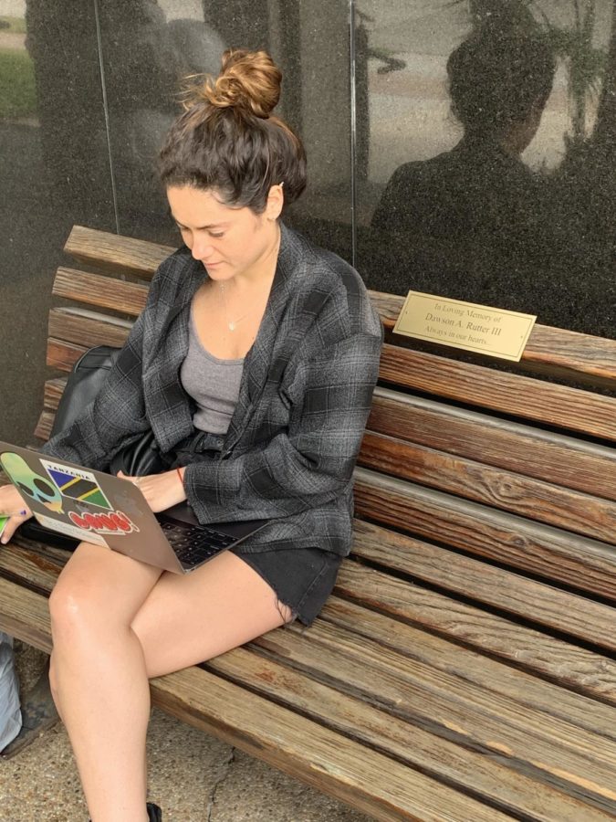 Loyola senior Devyn Koslen sits on the bench dedicated to Dawson Rutter III outside Miller Hall. Rutter passed away tragically in 2017 prior to graduating from Loyola. Photo credit: Chris Wiseman