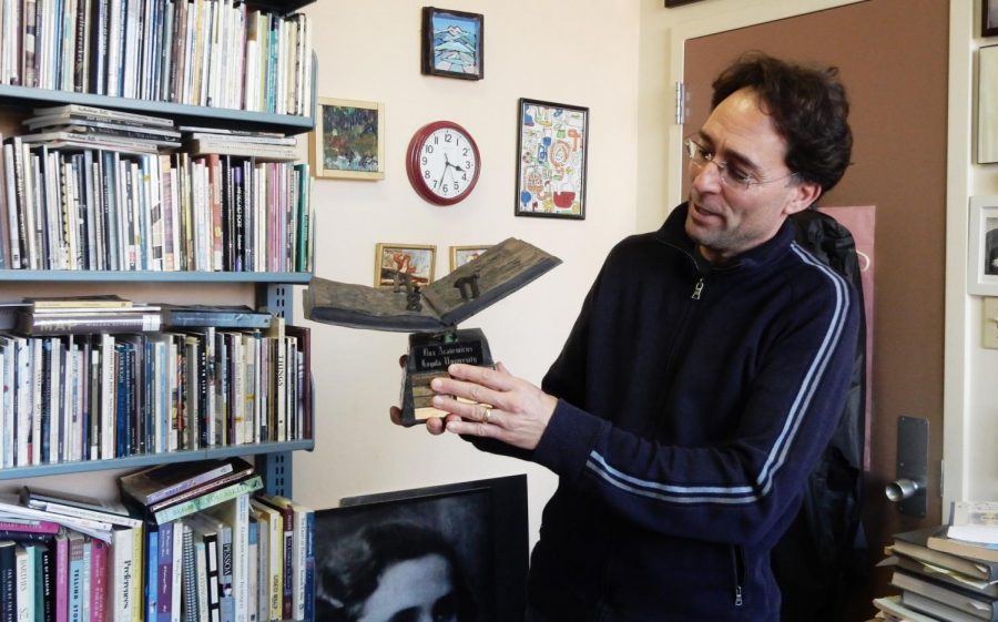 English professor and Dux Academicus Award winner Mark Yakich describes what his new trophy means to him. Pictured in his office on Jan. 23, 2020, he is surrounded by artwork from friends and books he enjoys as well as books he has written. Photo credit: Shadera Moore