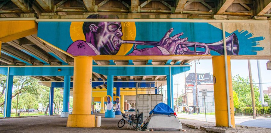An image under interstate 10 within the treme with a colorful mural on the bridge. Underneath the mural, a tent is located.