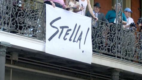 A group of people on a balcony holds a sign reading Stella!