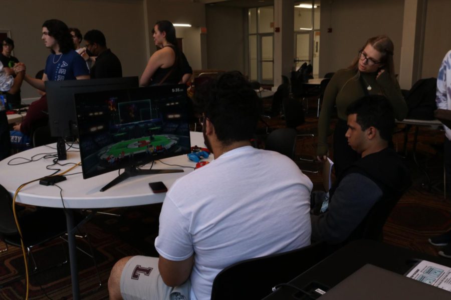 Two+esports+players+sit+in+front+of+a+screen+with+Smash+Bros+playing+on+it