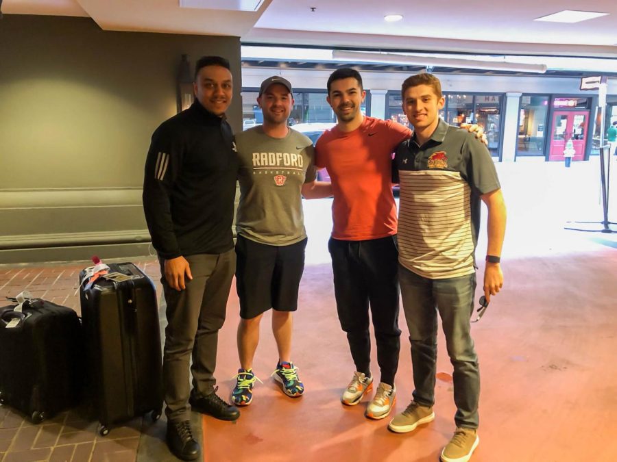 Fava and the coaches stand shoulder to shoulder together surrounded by suitcases at a hotel lobby
