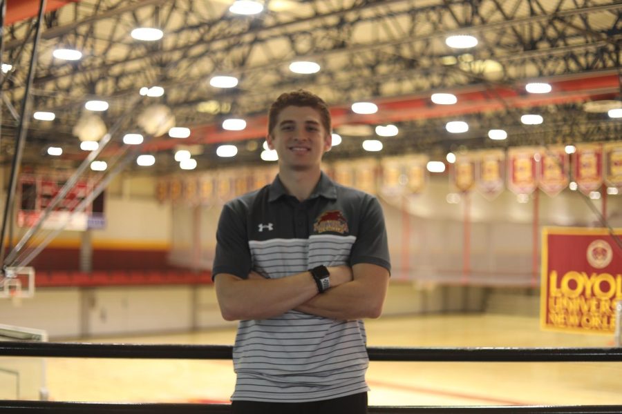 Andrew Fava stands with arms crossed in the University Sports Complex smiling in front of the basketball court