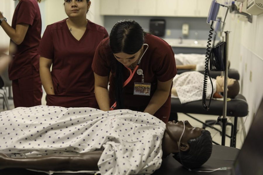 Nursing students practice checking vitals on a medical dummy.
