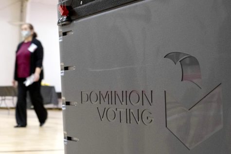 A worker passes a Dominion Voting ballot scanner while setting up a polling location at an elementary school in Gwinnett County, Ga., outside of Atlanta on Jan. 4, 2021. Testing before and after elections show the voting machines accurately tally the ballots, contradicting a relentless campaign of unfounded conspiracy theories that has undermined confidence in voting equipment throughout the U.S. 