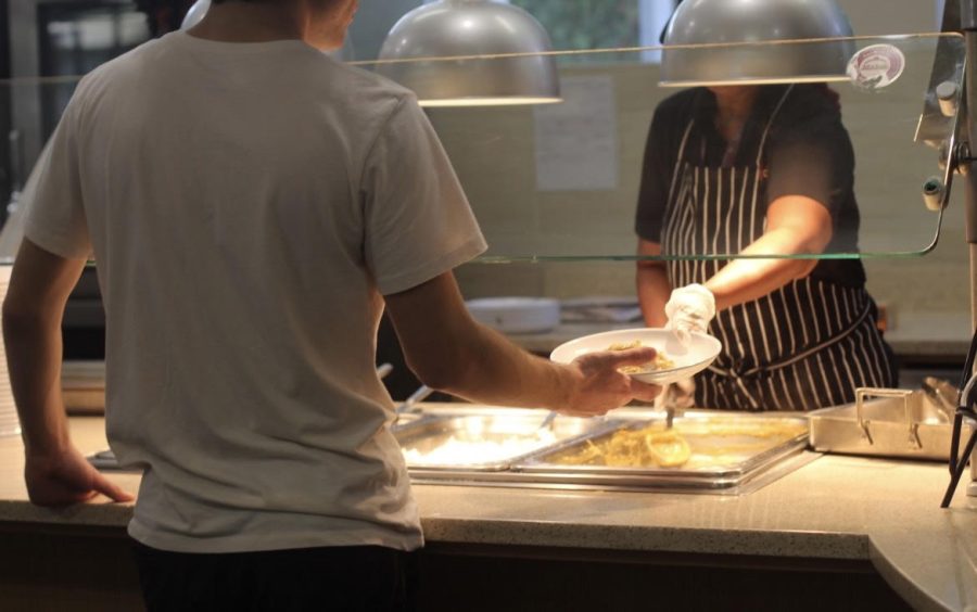 A student reaches out to grab food from a food service employee.