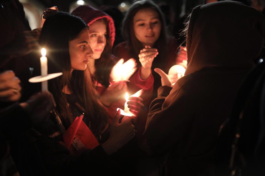Students stand in the dark holding candles.