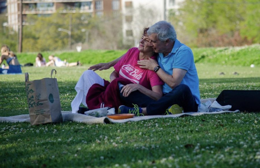 A older couple sits outside in the sun. They look happy.