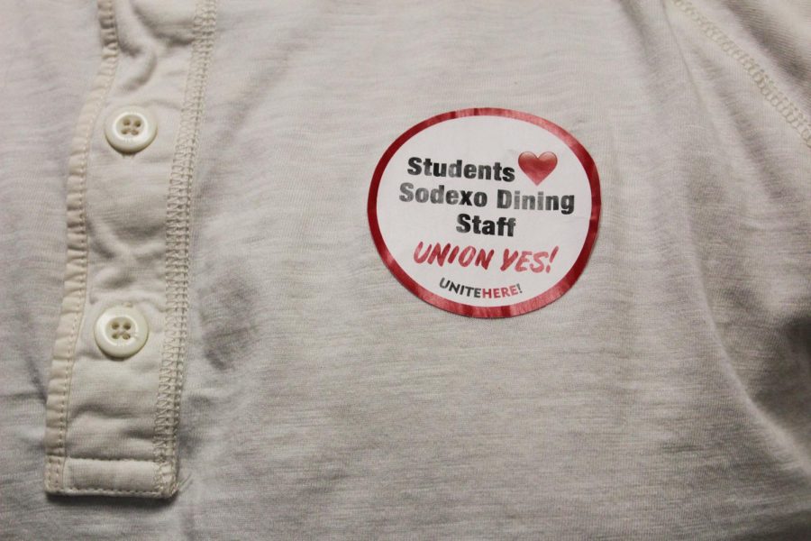 A person wears a sticker on their chest which reads Students (heart) dining staff, Union Yes!