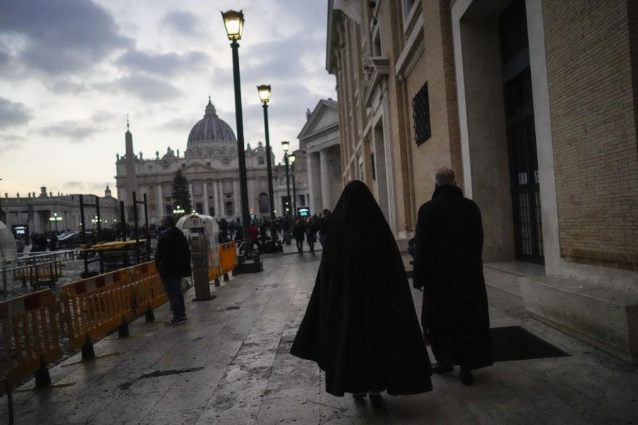A nun and a priest walk in black attire along a street