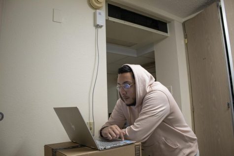 Loyola student Amid Bautista stands in front of his laptop in his dorm room. A new router installed by the school over break is attached to the wall behind him.
