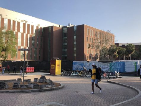 Student walking in front of the ongoing construction site. Monroe Hall can be seen in the background