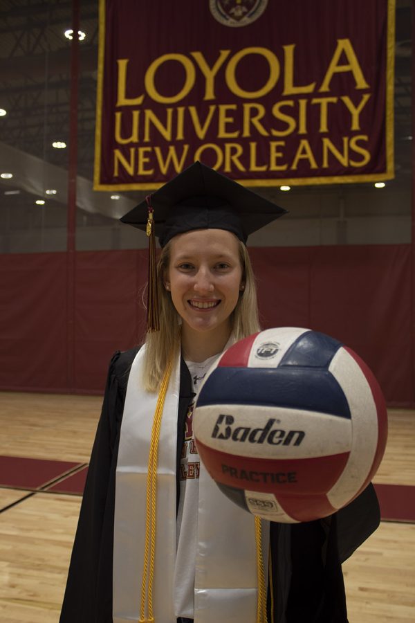 Senior mass communication major Brittany Cooper stands holding a volleyball with her graduation cap and gown.