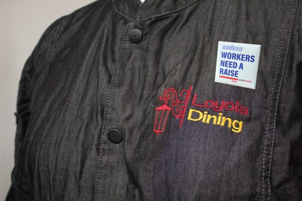 Loyola Dining Sodexo worker in uniform with a pin saying Sodexo workers need a raise. 