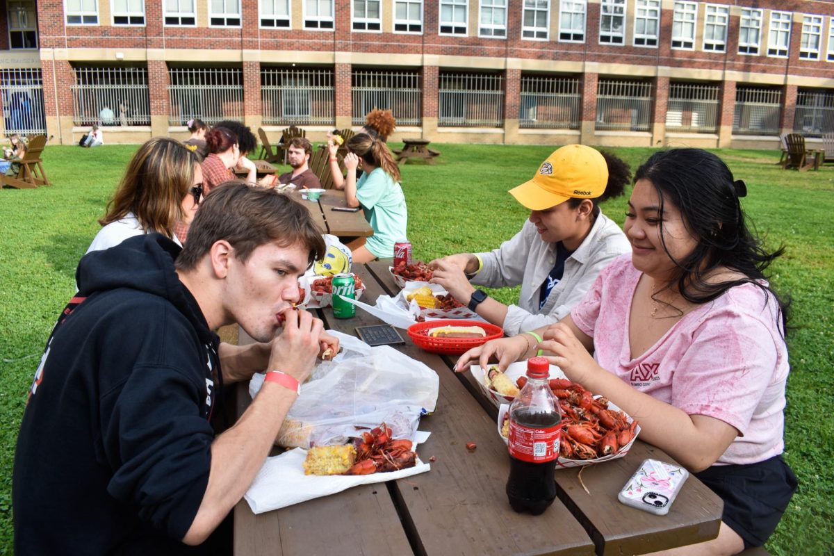 Seniors Augie Lodholz (left) and Stephanie Oblena (far right) eat crawfish on the residential lawn on March 15, 2024. 