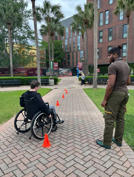 Psychology freshman and member of Disabled Students Assembly KC Crawford leads design senior Ace McConnell in the wheelchair obstacle course on April 11, 2024. The course was created to allow the Loyola community to experience what navigating life in a wheelchair is like.