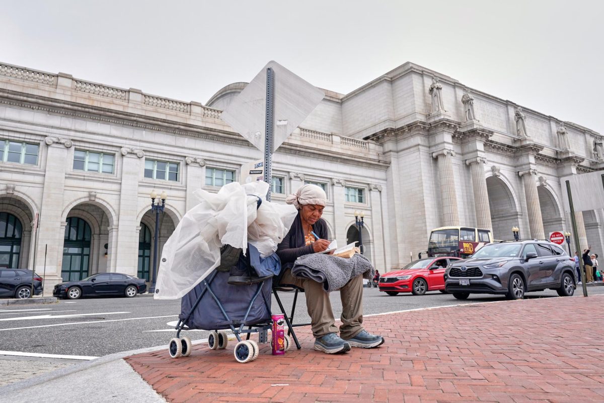 A homeless person sits on a sidewalk in front of Union Station as National Guard soldiers patrol nearby Wednesday, Aug. 20, 2025, in Washington. 